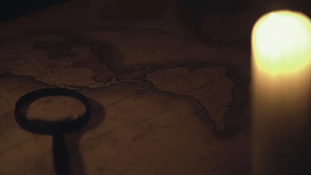 A candle, an old key-shaped magnifier and a map on a dark table