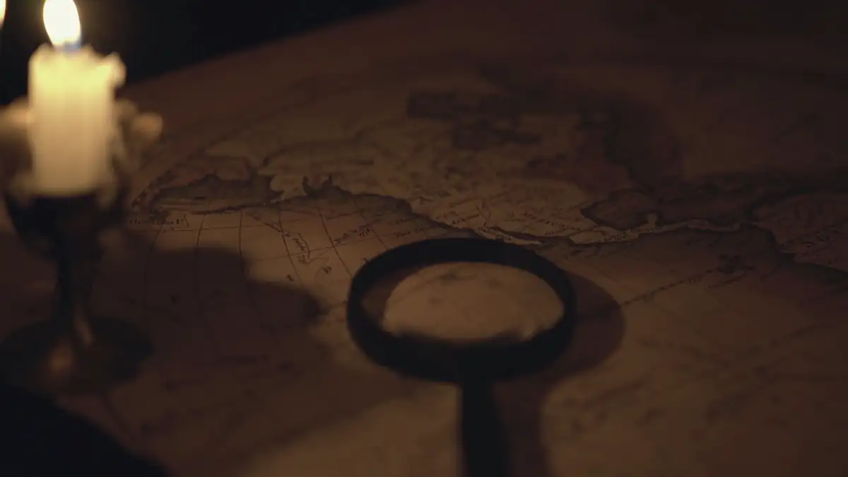A candle, an old key-shaped magnifier and a map on a dark table