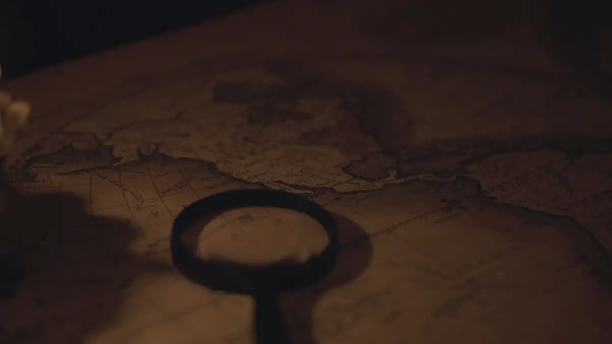 A candle, an old key-shaped magnifier and a map on a dark table