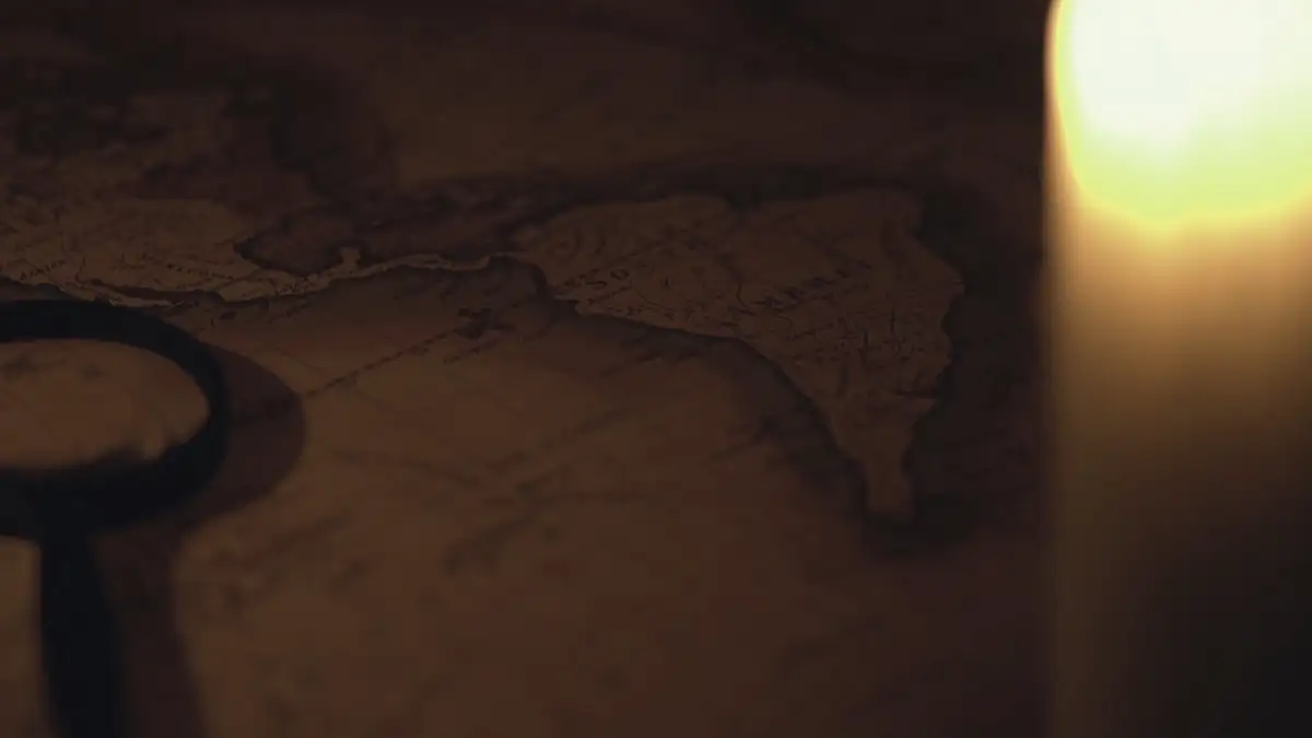 A candle, an old key-shaped magnifier and a map on a dark table